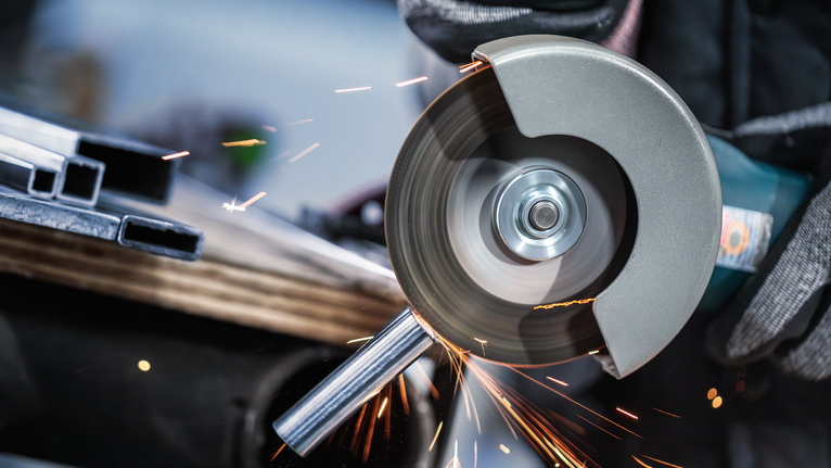 안전 장비를 착용한 사람이 각도 분쇄기를 사용하여 금속 파이프를 자릅니다.