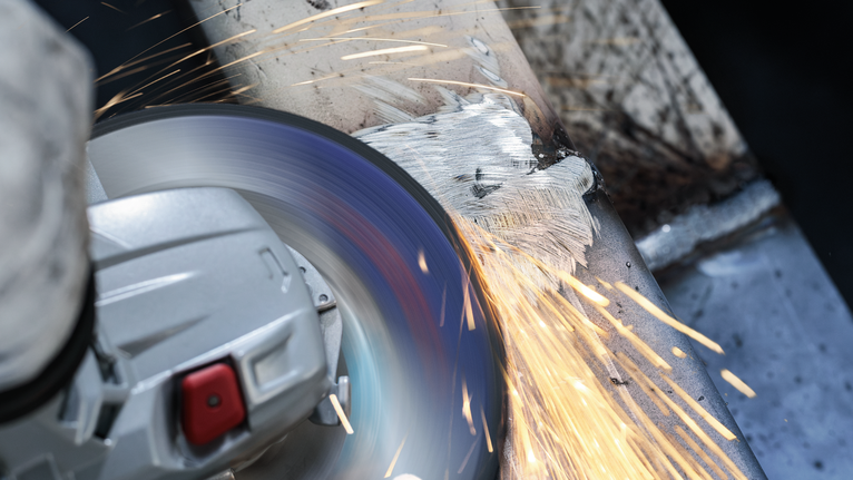 안전 장비를 착용한 사람이 금속 표면을 갈아서 밝은 불꽃을 낸다.