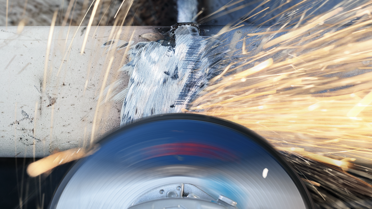 밝은 불꽃을 튀기며 금속 파이프를 매끄럽게 다듬는 연삭 도구.