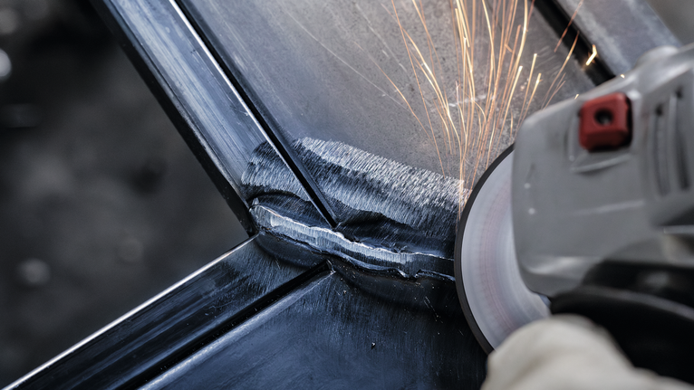 안전 장비를 착용한 사람이 금속 용접부를 갈아서 불꽃이 생깁니다.