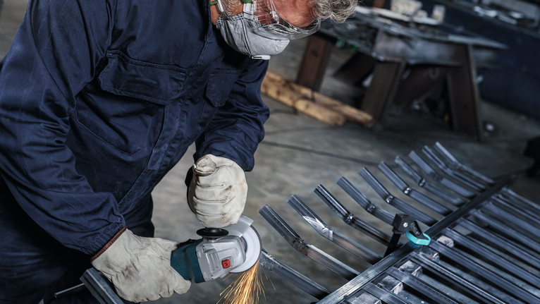 안전 장비를 착용한 사람이 금속 막대를 갈아서 불꽃이 튀는 모습.