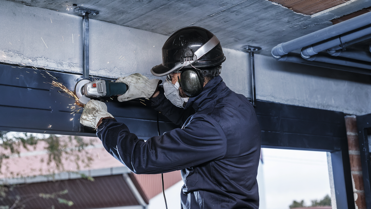 안전 장비를 착용한 사람이 금속 빔을 갈아서 불꽃이 난다.