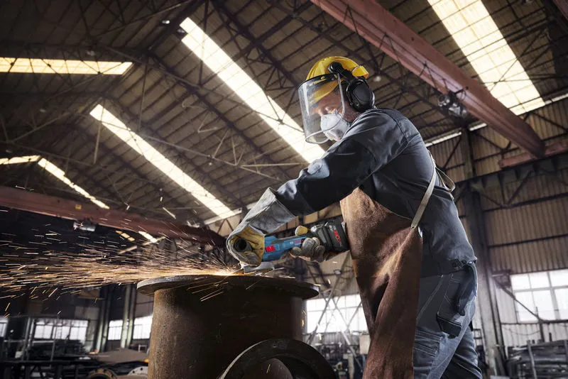 안전 장비를 착용한 사람이 무선 각도 분쇄기를 사용하여 금속을 절단하면서 불꽃을 발생시킵니다.