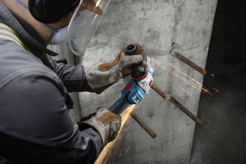 안전장비를 착용한 사람이 콘크리트 벽의 노출된 철근을 갈아내고 있습니다.