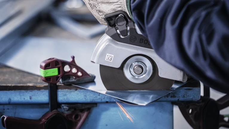 안전 장비를 착용한 사람이 원형 톱으로 금속판을 자르면서 불꽃이 튀는 모습입니다.