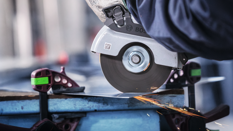 안전 장비를 착용한 사람이 각도 연삭기를 사용하여 금속판을 자릅니다.