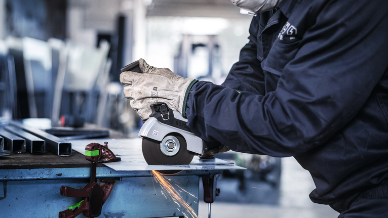 안전 장비를 착용한 사람이 금속판을 갈아서 불꽃이 난다.