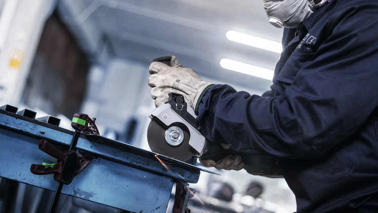 안전 장비를 착용한 사람이 각도 분쇄기로 금속을 자르면서 불꽃을 일으킵니다.