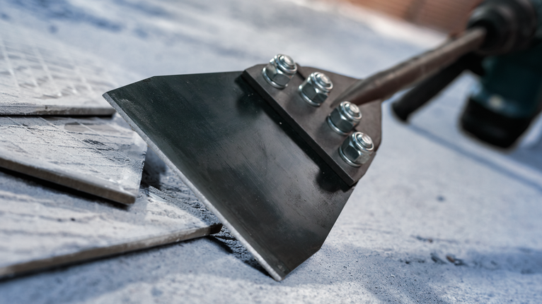 넓은 끌날로 콘크리트 표면에서 바닥 타일을 제거합니다.