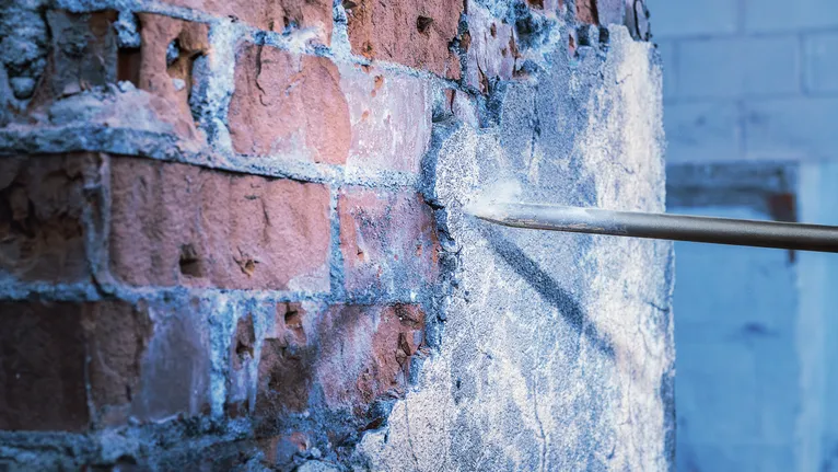 끌로 벽돌 벽에서 콘크리트 석고를 제거합니다.