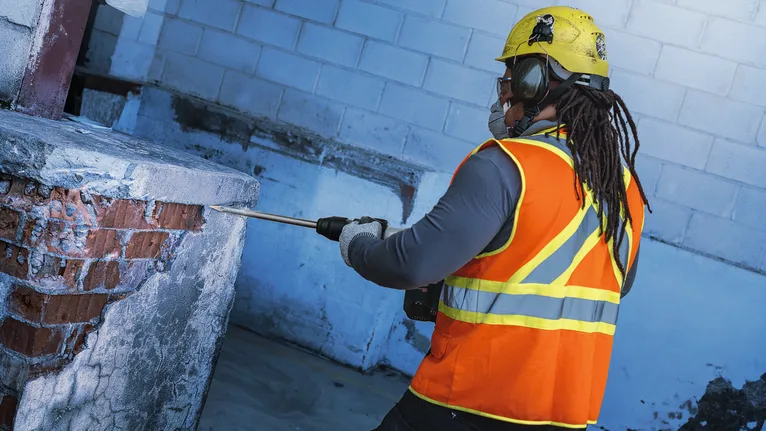 안전 장비를 착용한 사람이 철거 도구를 사용하여 콘크리트와 벽돌을 부수고 있습니다.
