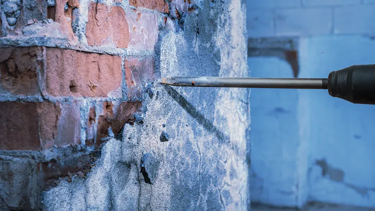 드릴 끌로 벽돌 벽에서 콘크리트를 부수고 있습니다.