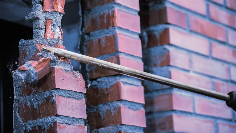 철거 중에 끌 도구로 붉은 벽돌 벽을 부수는 모습입니다.