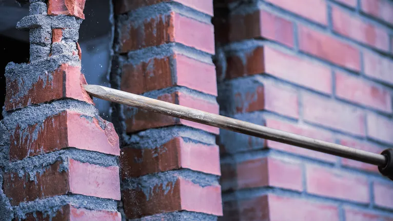 붉은 벽돌 벽을 부수고 있는 끌 도구.