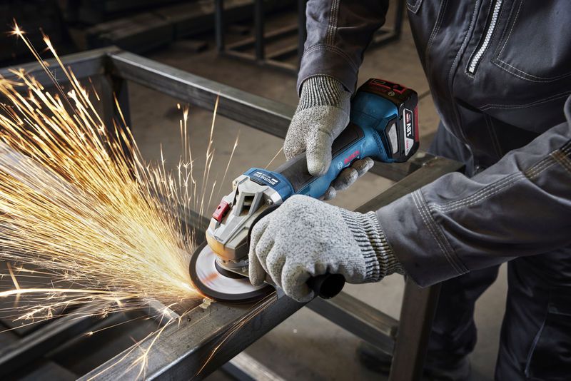 안전 장비를 착용한 사람이 각도 그라인더로 금속 빔을 갈아내고 있습니다.