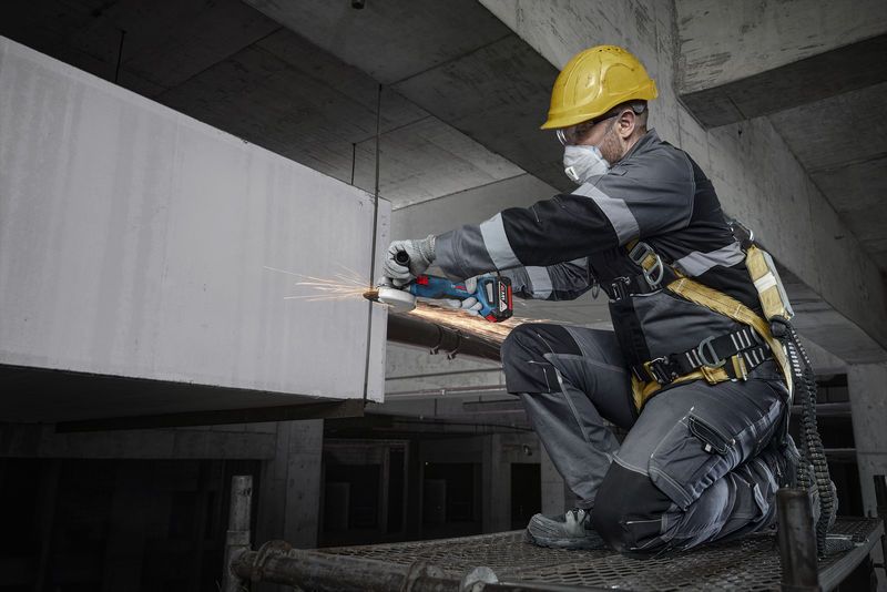 안전 장비를 착용한 사람이 건설 현장에서 전동 공구를 이용해 콘크리트를 갈고 있습니다.