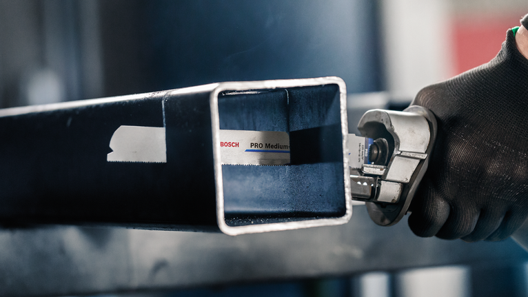 안전 장비를 착용한 사람이 톱을 사용하여 금속 사각형 튜브를 자릅니다.