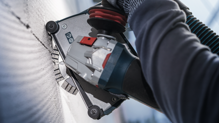 안전 장비를 착용한 사람이 전동 공구로 벽을 갈고 있습니다.