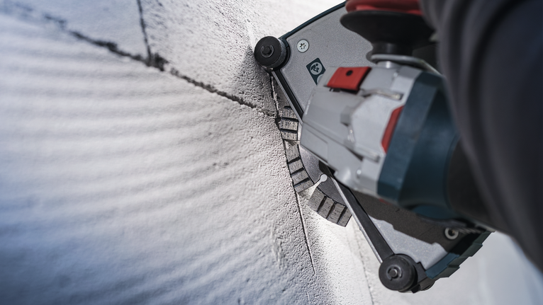 안전 장비를 착용한 사람이 전동 공구를 사용하여 콘크리트에 직선 홈을 파고 있습니다.