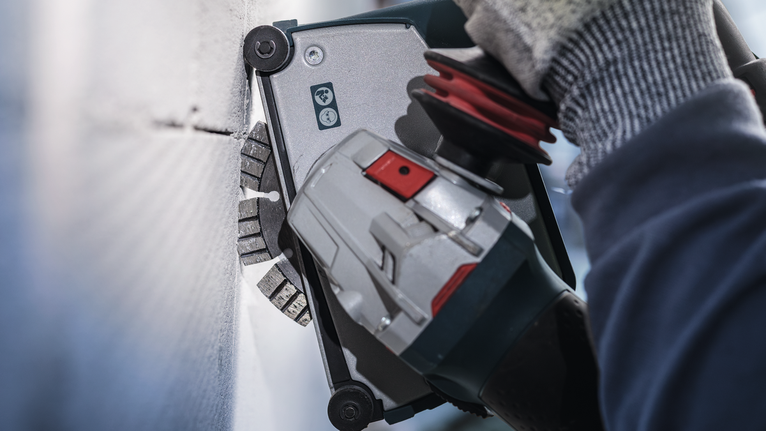 안전 장비를 착용한 사람이 전동 공구를 사용해 벽을 자르고 있습니다.