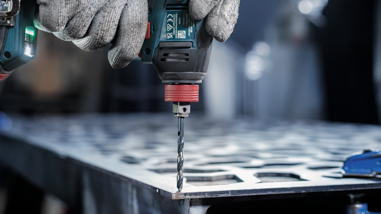 안전 장비를 착용한 사람이 금속판에 구멍을 뚫고 있습니다.