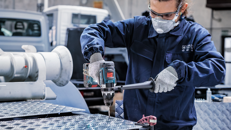 안전 장비를 착용한 사람이 산업 현장에서 금속판에 구멍을 뚫고 있습니다.