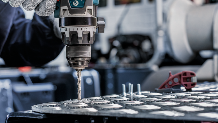 안전 장비를 착용한 사람이 금속판에 구멍을 뚫고 있습니다.