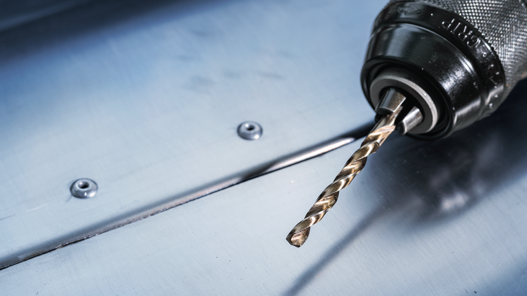 강철판 위에 금속 드릴 비트가 올려진 전기 드릴입니다.