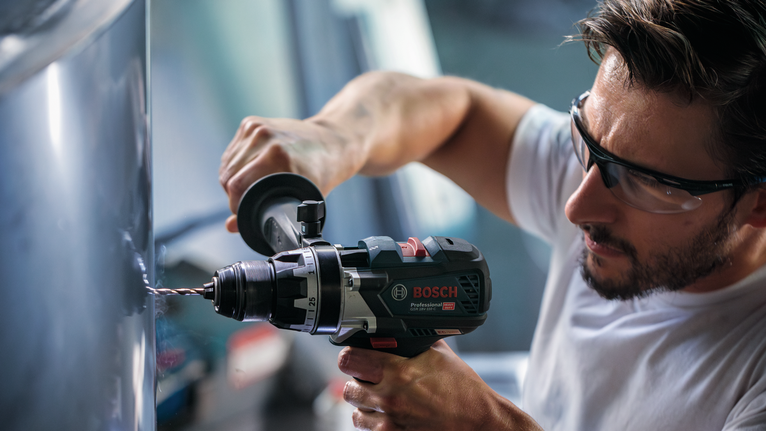 안전 장비를 착용한 사람이 전동 공구로 금속에 구멍을 뚫고 있습니다.