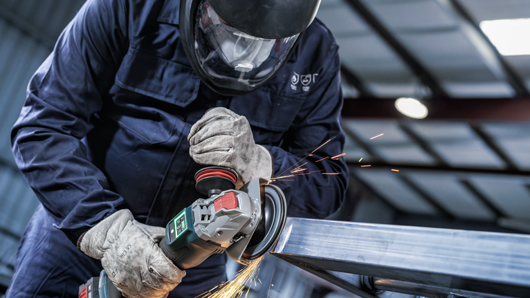 안전 장비를 착용한 사람이 금속을 갈아서 불꽃이 난다.