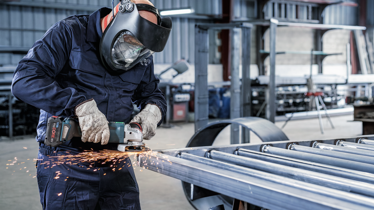 안전 장비를 착용한 사람이 작업장에서 금속을 갈아서 불꽃을 일으킨다.