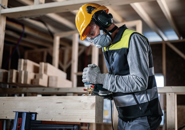 안전 장비를 착용한 사람이 건설 현장에서 톱을 사용하여 나무를 자르고 있습니다.