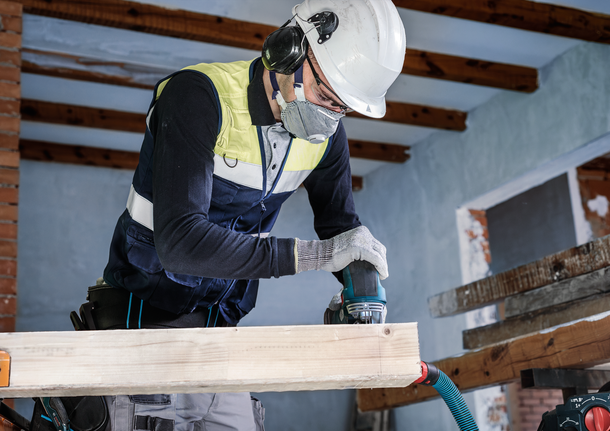 안전 장비를 착용한 사람이 전동 공구로 나무 들보를 연마하고 있습니다.