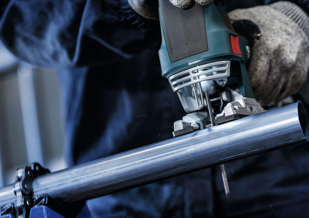 안전 장비를 착용한 사람이 퍼즐을 사용하여 금속 파이프를 자릅니다.