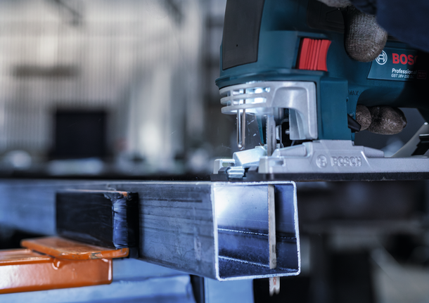 안전 장비를 착용한 사람이 퍼즐을 조종해 금속 막대를 자르고 있습니다.