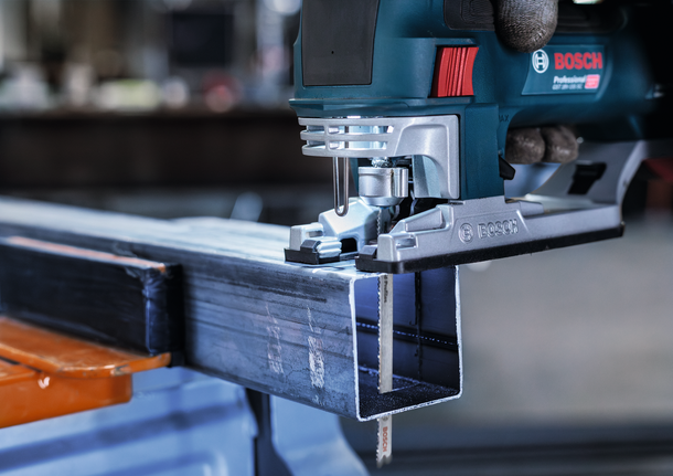 안전 장비를 착용한 사람이 퍼즐 톱으로 금속 막대를 자릅니다.