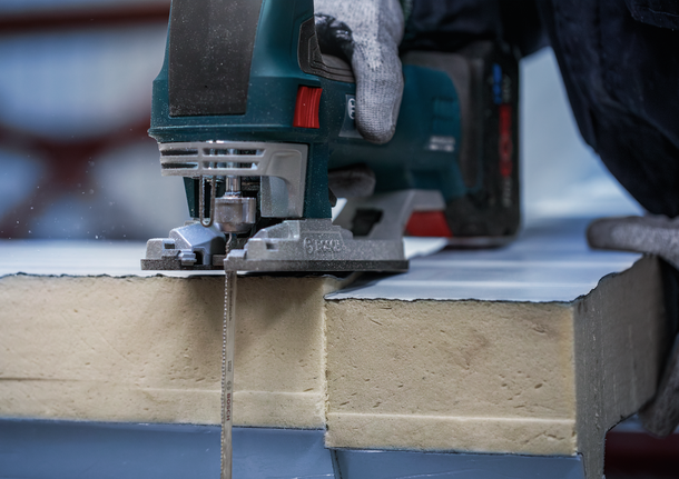 안전 장비를 착용한 사람이 톱으로 단열 보드를 자르고 있습니다.