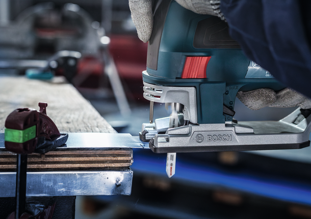 안전 장비를 착용한 사람이 톱으로 금속판을 자르고 있습니다.