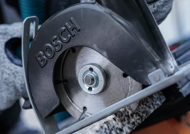 안전 장비를 착용한 사람이 원형 톱으로 돌을 자르고 있습니다.