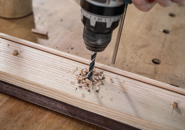 드릴을 사용하여 나무판에 구멍을 뚫는 사람.