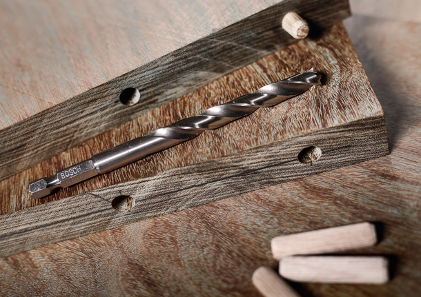 나무 판자 위에 드릴 비트를 놓고, 근처에 구멍을 뚫고, 헐거운 막대를 놓습니다.