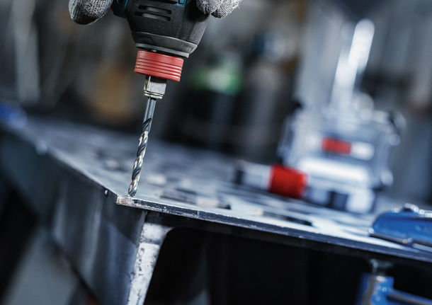 안전 장비를 착용한 사람이 금속판에 구멍을 뚫고 있습니다.