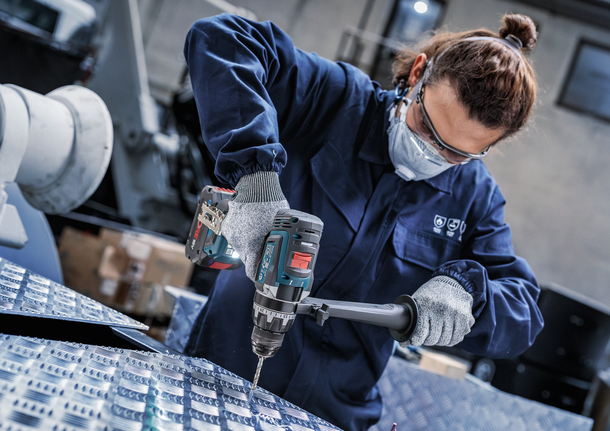 안전 장비를 착용한 사람이 금속판에 구멍을 뚫고 있습니다.