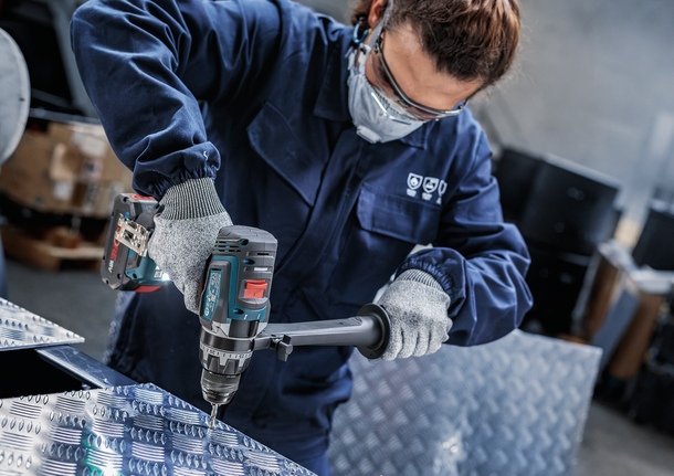 안전 장비를 착용한 사람이 금속판에 구멍을 뚫고 있습니다.