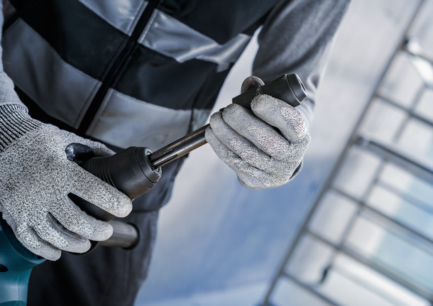 안전 장비를 착용한 사람이 전동 공구에 금속 비트를 부착하고 있습니다.