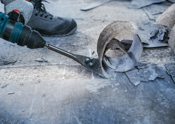 안전 장비를 착용한 사람이 전동 공구를 사용하여 바닥재를 제거합니다.