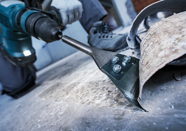 안전 장비를 착용한 사람이 전동 공구를 사용하여 바닥재를 제거합니다.