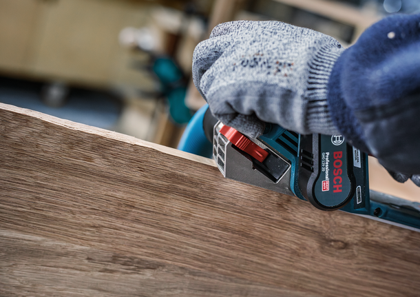 안전 장비를 착용한 사람이 전동 공구를 이용해 나무판의 가장자리를 매끄럽게 다듬고 있습니다.