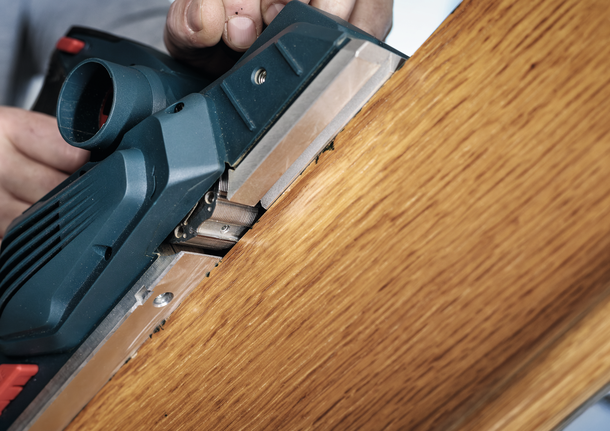 한 사람이 전동 刨削기를 사용하여 나무판의 가장자리를 매끄럽게 다듬고 있습니다.