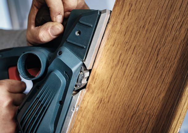 한 사람이 전동 刨削기를 사용하여 나무판의 가장자리를 매끄럽게 다듬고 있습니다.